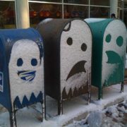 Three mailboxes covered in snow with ghosts carved into them