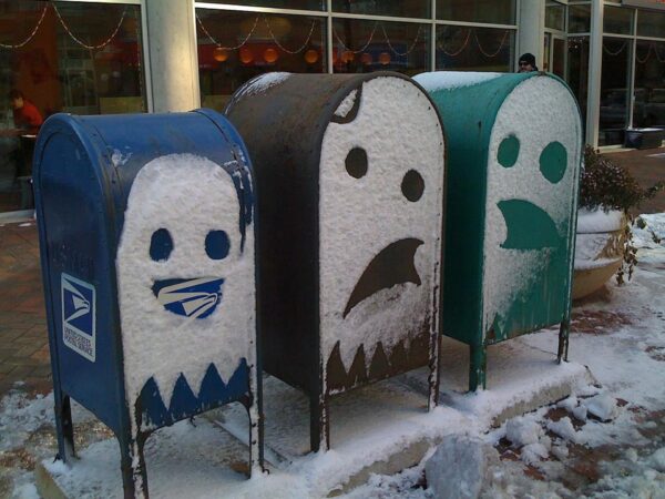 Three mailboxes covered in snow with ghosts carved into them