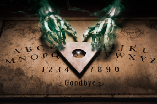 Glowing skeleton hands using a planchette on a Ouija board