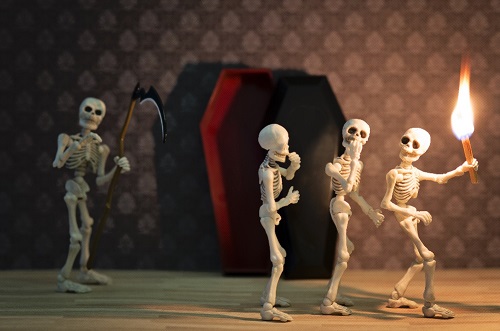 Three skeletons in front of a coffin with matchstick torch and skeleton reaper behind them