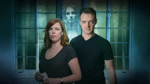 Amy Bruni and Adam Berry in front of a window with a ghost face