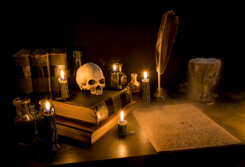 Dark creepy desk with candles, quill and pen and skull on books