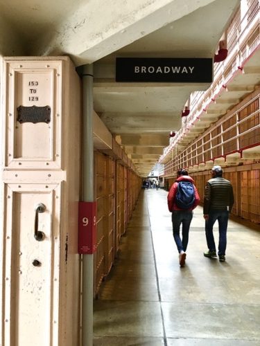 Two people walking down Broadway at Alcatraz with view of cell locking and operating box on wall
