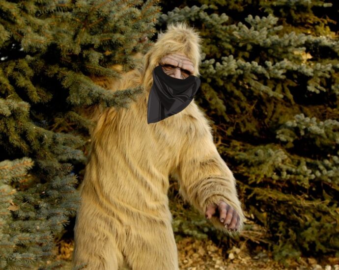 Bigfoot peeking out from behind pine tree wearing a blask mask bandana