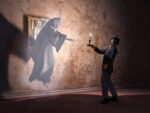 Ghost hovering in a hallway in front of man holding candle