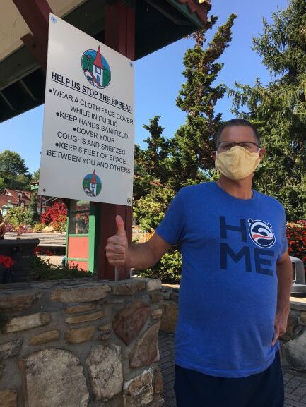 Man in mask posing in front of COVID-19 travel guidelines sign in Helen, Georgia