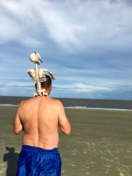 Man with skeleton on his shoulders at beach looking at rainbow