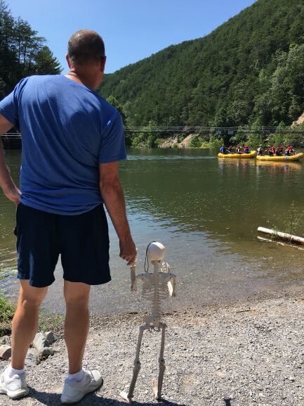 Man holding tiny skeleton's hand while watching white water rafters on the Ocoee