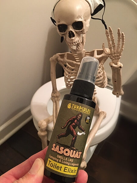 Skeleton on toilet with a bottle of Turdcules Bigfoot toilet elixir