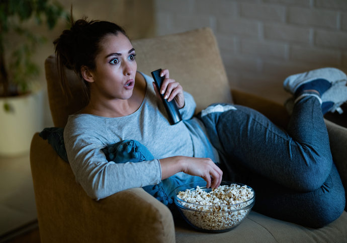 Woman eating popcorn on a couch while she binge watches TV
