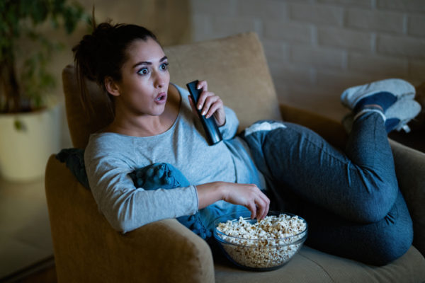 Woman eating popcorn on a couch while she binge watches TV