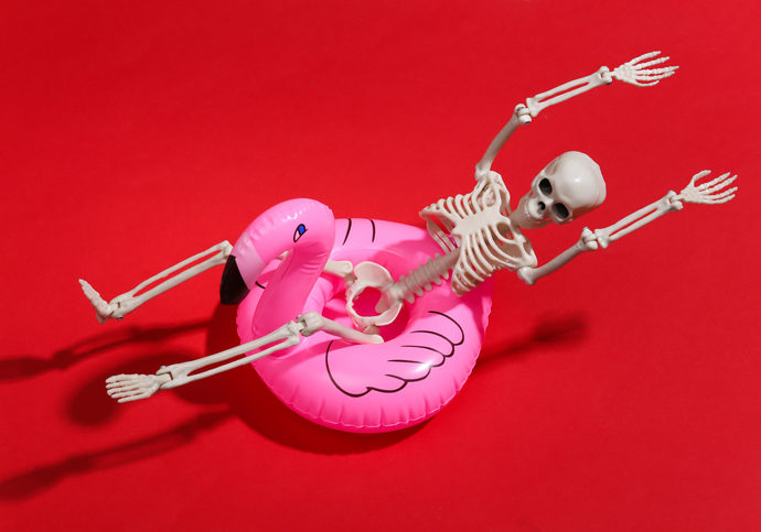 Toy skeleton with inflatable flamingo on red bright background. Halloween theme. Beach vacation concept. Summer rest.