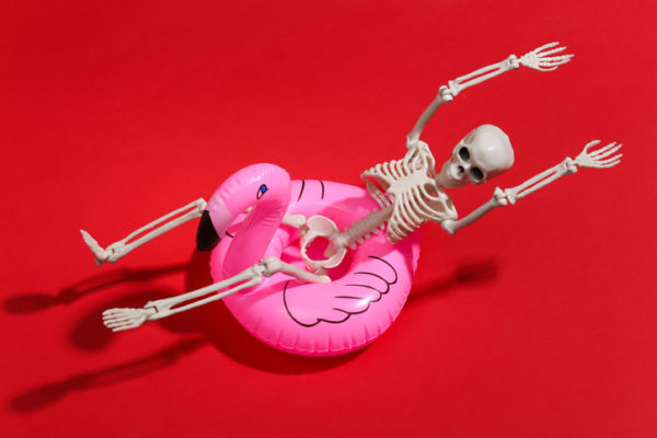 Toy skeleton with inflatable flamingo on red bright background. Halloween theme. Beach vacation concept. Summer rest.
