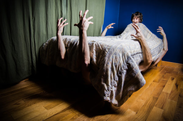 Young boy hiding in bed with monsters under bed