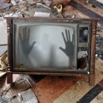 Ghostly hands pushing on screen from inside haunted TV