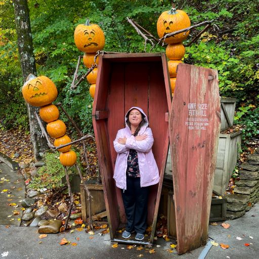 Woman in pink raincoat posing in coffin at Dollywood's Pumpkin LumiNights