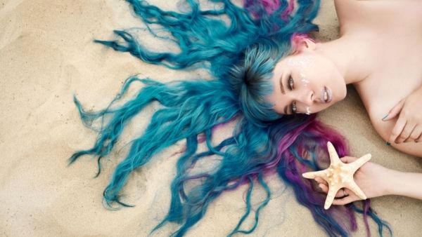 Mermaid laying on sand holding starfish with blue hair fanned out