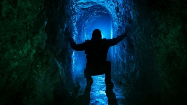 Silhouette of a man crouched down in a cave exploring underground