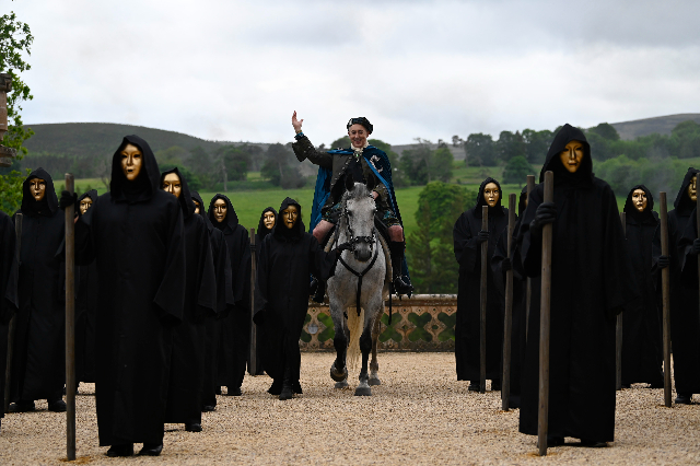 Alan Cumming on horseback amidst cloaked and masked Traitors