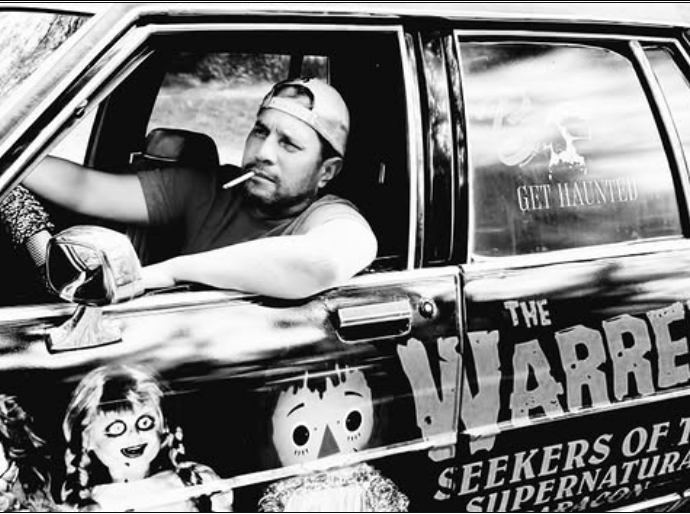 Dan Rivera in car smoking cigarette with Annabelle doll and Warren Occult Museum painted on the door