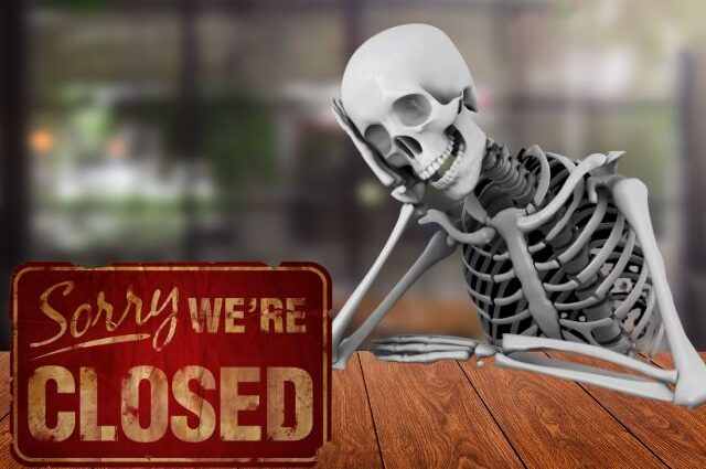 Skeleton sitting at restaurant table with a sorry we're closed sign to announce closing