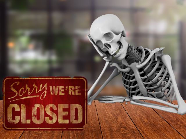 Skeleton sitting at restaurant table with a sorry we're closed sign to announce closing